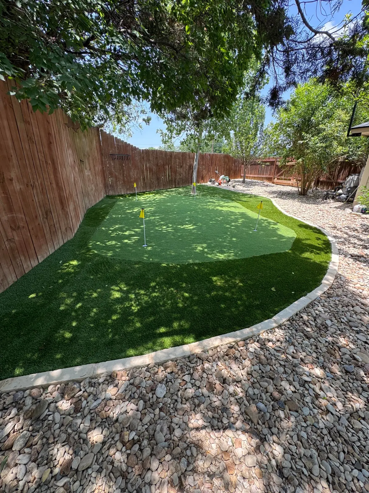 Backyard putting green with stone edging and river rock
